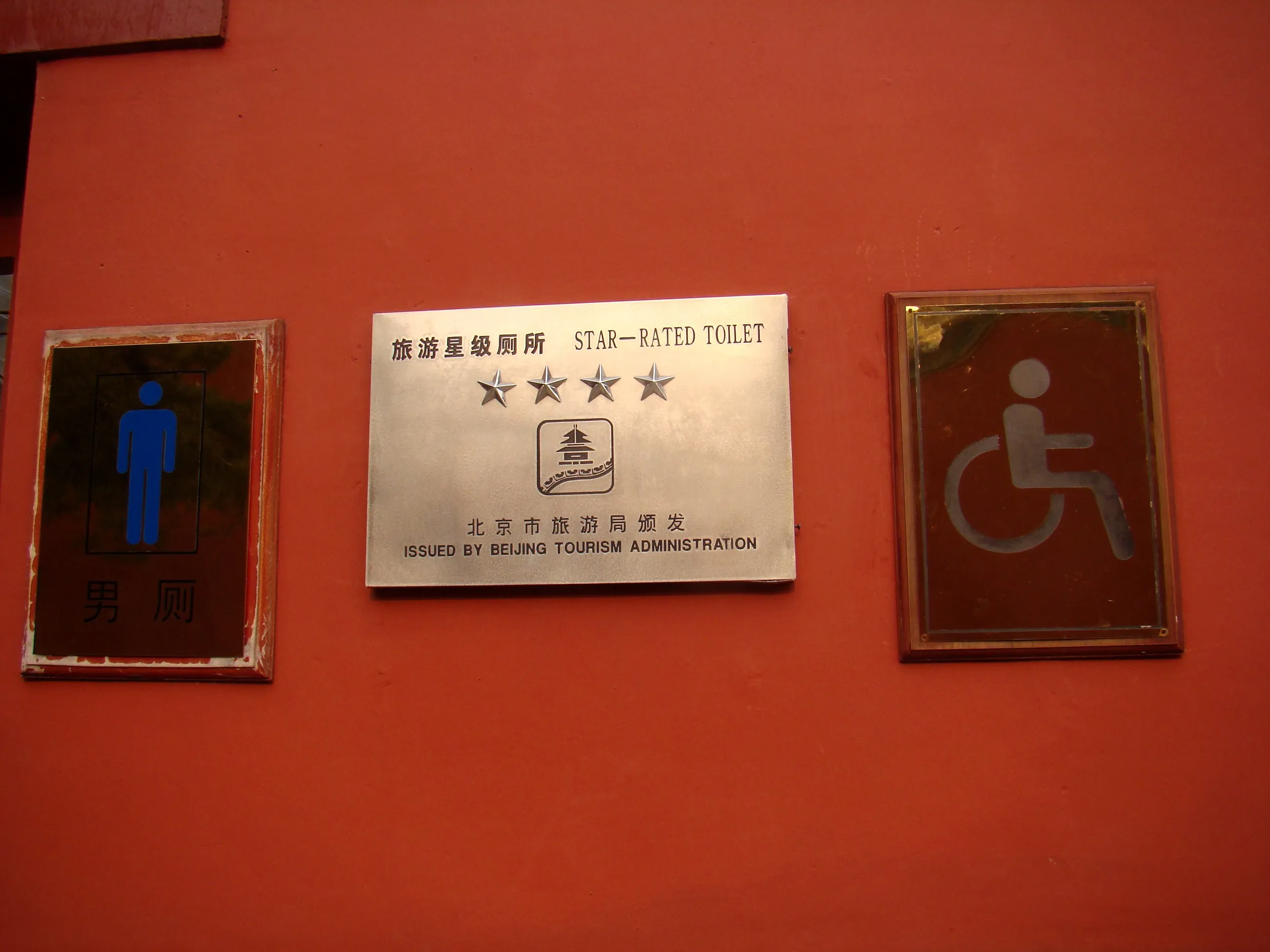 A four-star 'star-rated toilet' placard issued by the Beijing Tourism Administration on a red wall at the Forbidden City, beside men's-room and accessibility signs