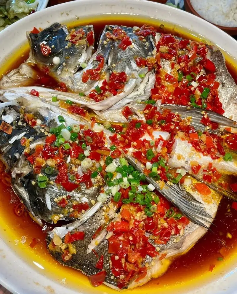 Steamed Fish Head with Chopped Chili — a massive fish head buried under bright red fermented chilies